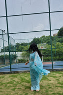 aqua green chiffon saree with white leaf print, model walking outdoors back profile