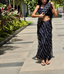 Black chiffon leheriya saree with gold border, model standing outdoors