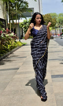 Black chiffon leheriya saree with gold border, model candidly walking outdoors