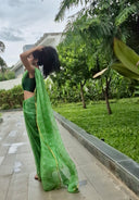 Green chiffon leheriya saree with gold border, model sitting outdoors